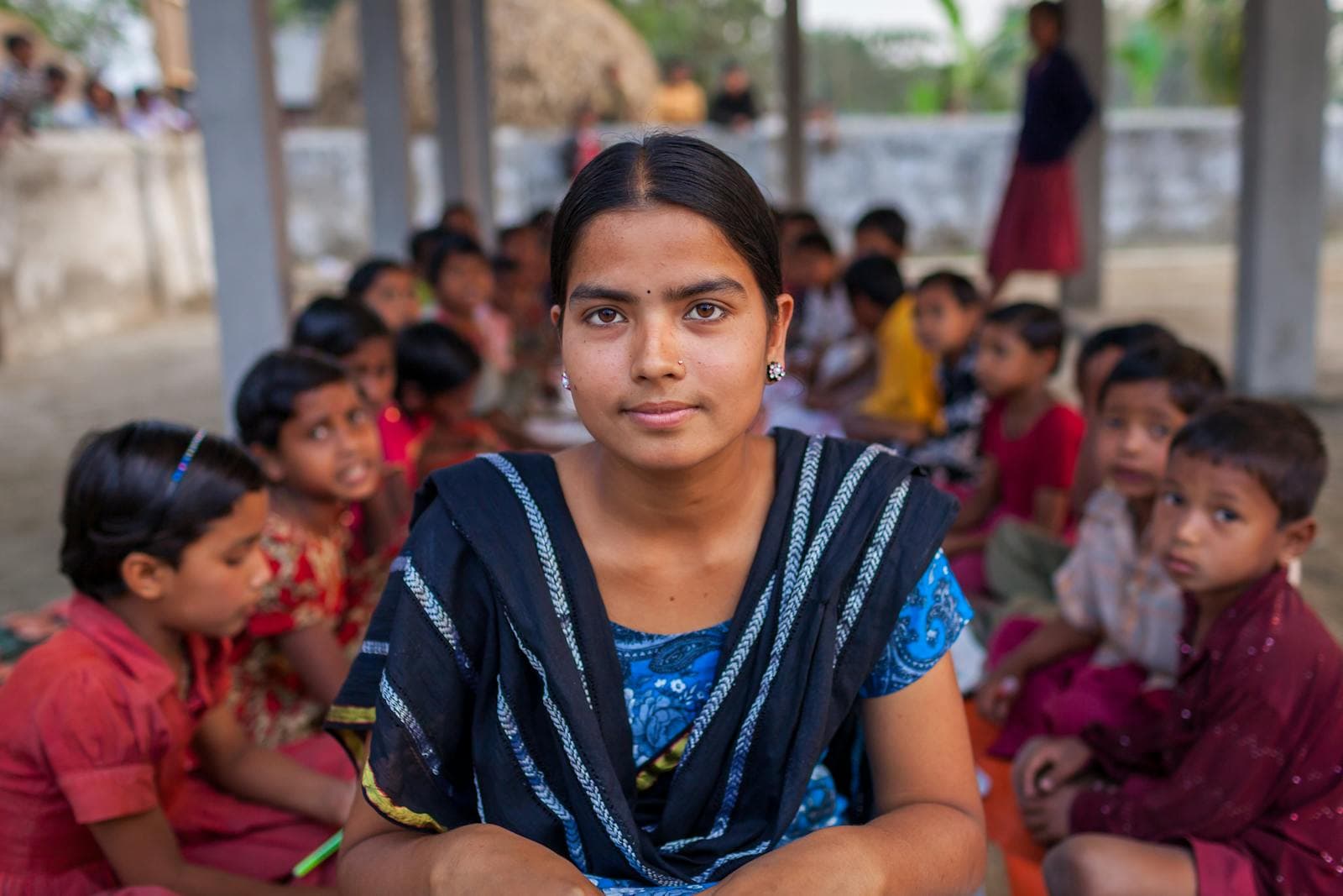 A teacher sitting with her students in an outdoor classroom during a board visit