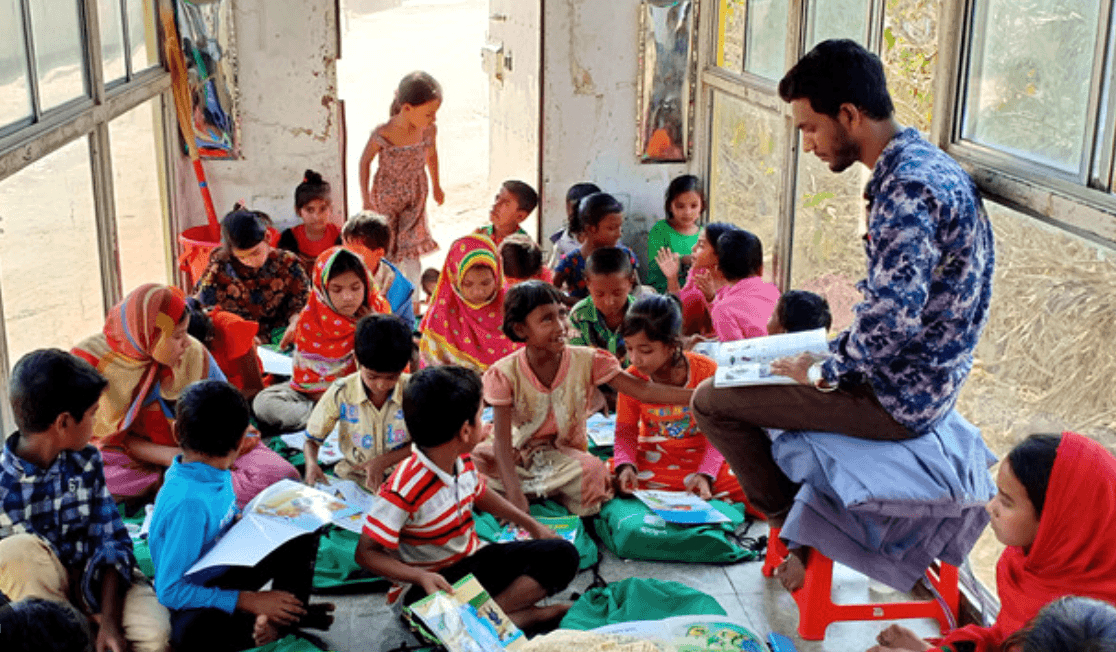 Students in a Bangladesh classroom hold up their drawings beside their teacher