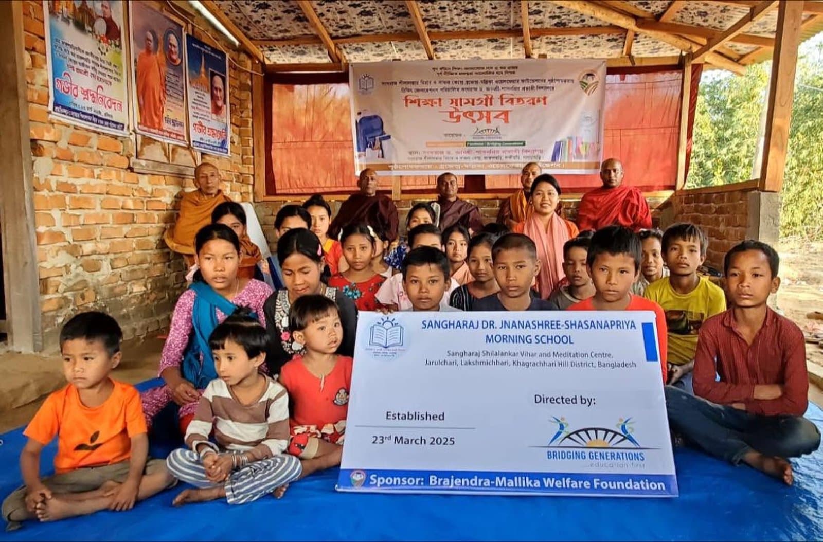 Students, monks, and staff gather at the opening of a morning school in the Chittagong Hill Tracts, holding a dedication sign