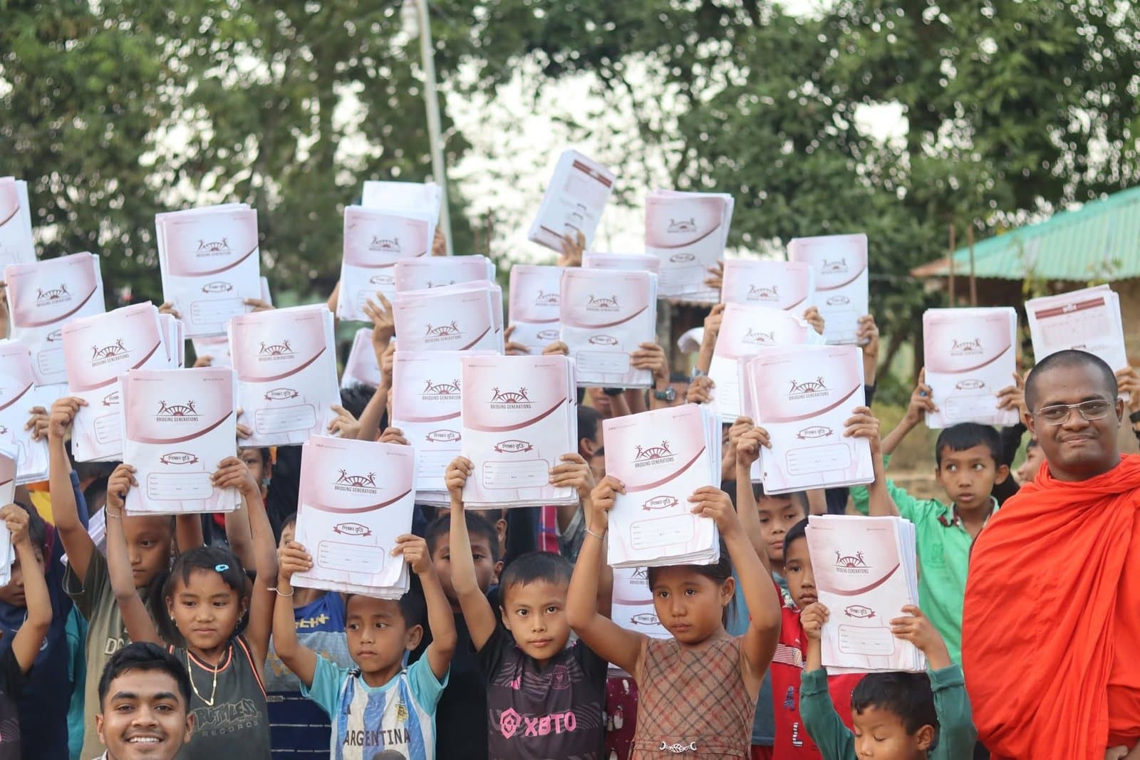 Students hold up notebooks printed with the Bridging Generations logo