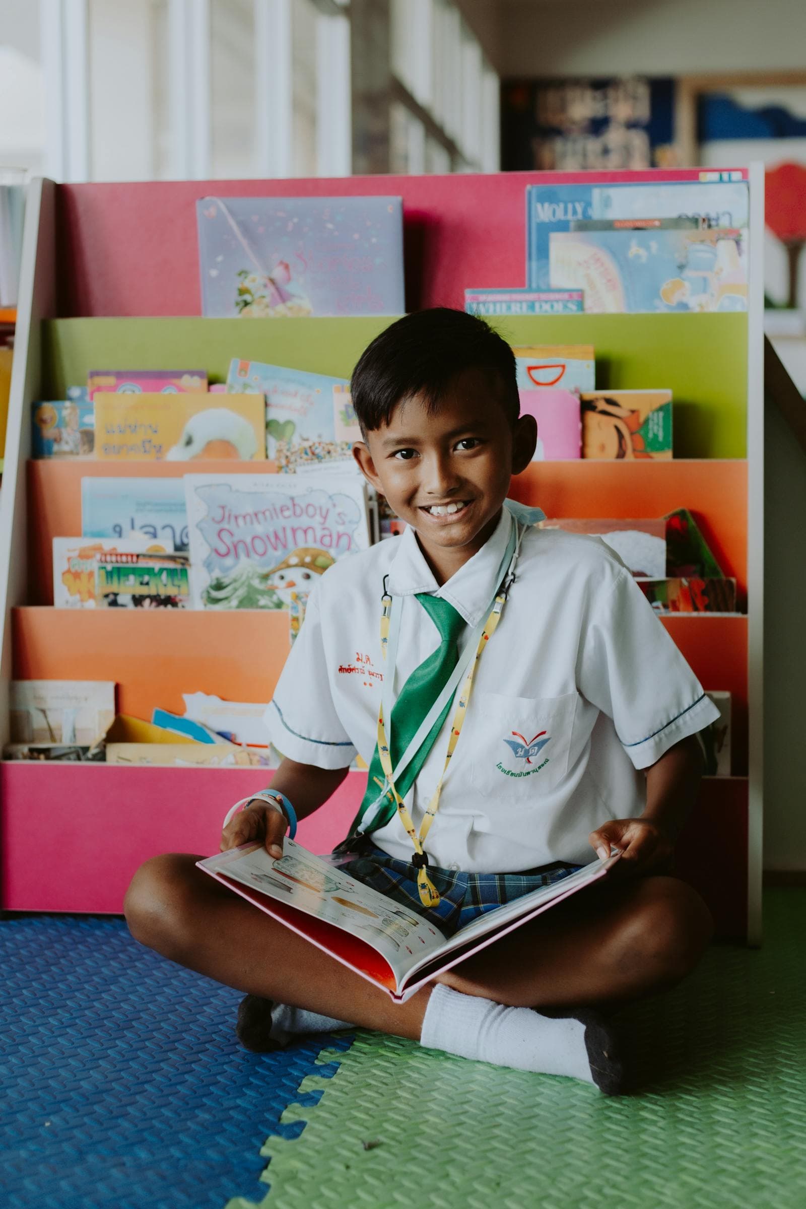 A schoolboy in uniform sits in a library corner reading a book
